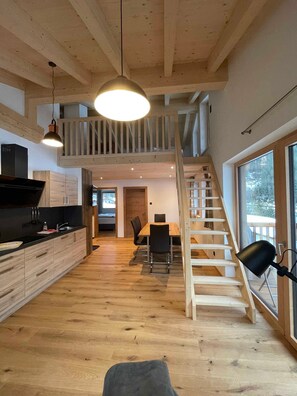 Eine moderne Küche mit Holzausstattung, ein Essbereich mit Tisch und Stühlen sowie eine Treppe, die in eine obere Etage führt.