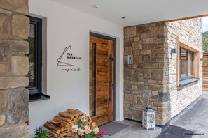 Pared exterior de piedra, una puerta de madera y una ventana con un motivo de montaña en la pared.