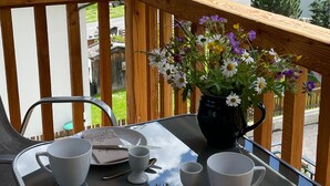 A balcony with a table set for two, a vase of flowers, and a view of a forested area. - Apartment Edelweiss - TUX MOUNTAIN apart (Juns)