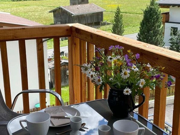 Un balcón con baranda de madera, una mesa con un florero y una silla.