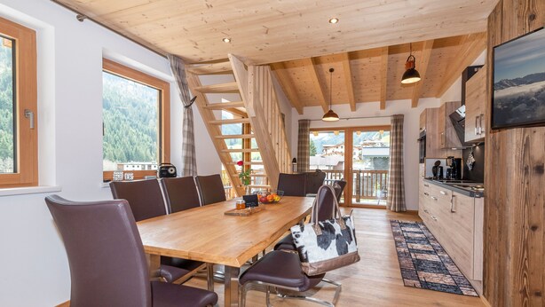 A wooden interior with a dining table, chairs, a kitchen area, and large windows offering a mountain view. - Apartment Edelweiss - TUX MOUNTAIN apart (Juns)