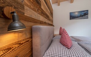 Ein gemütliches Zimmer mit einem Holzkopfteil, einer Lampe, karierten Kissen und einem gerahmten Bild an der Wand.