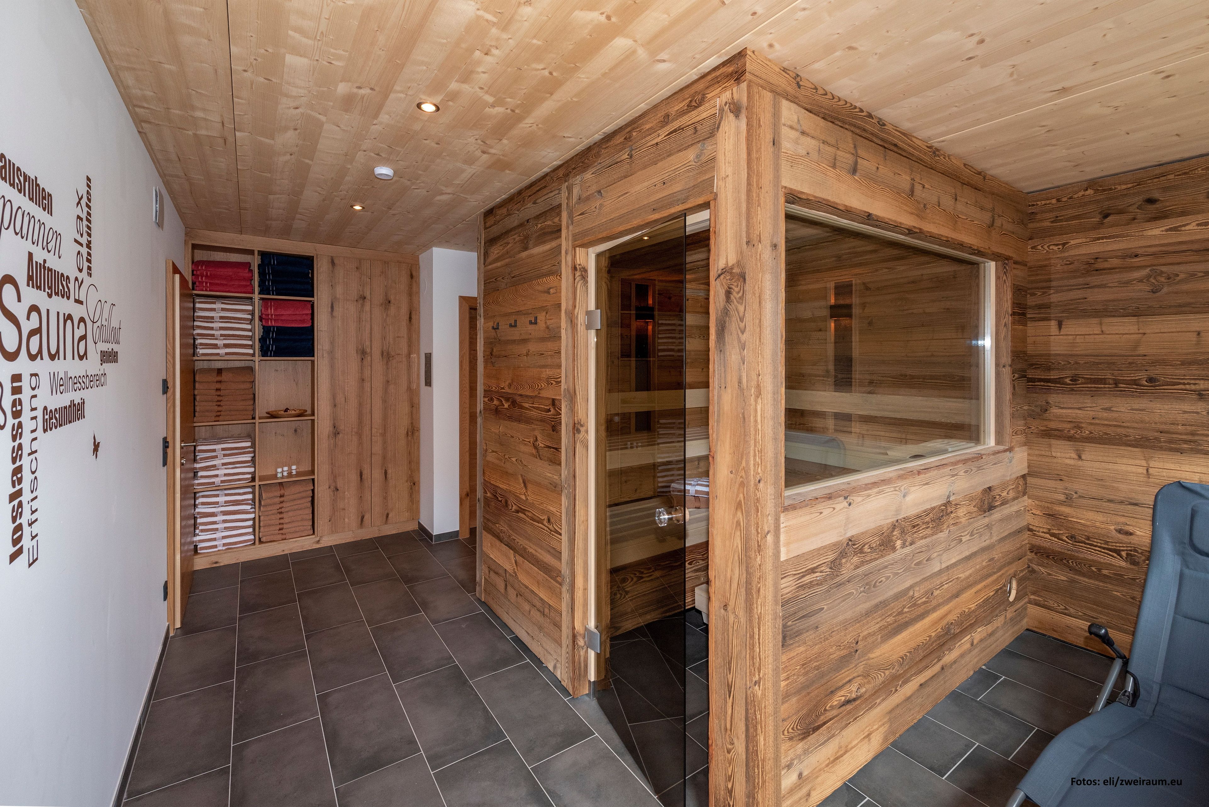 Interior de madera con una sauna, una puerta de cristal y una silla azul.