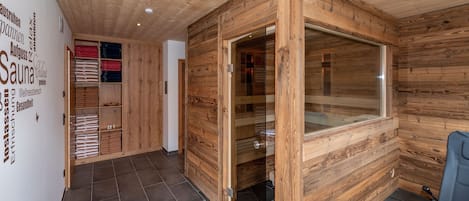 Interior de madera con una sauna, una puerta de cristal y una silla azul.