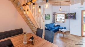 Ein modernes Interieur mit einer Holztreppe, einem blauen Sofa, einem Esstisch und hängenden Leuchten.
