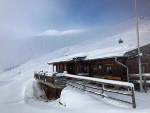 A wooden building with a snow-covered roof and a wooden deck. - Apartment Enzian - TUX MOUNTAIN apart (Juns)