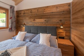 A bedroom with a wooden headboard, checkered bedding, a bedside table, and a window with curtains.