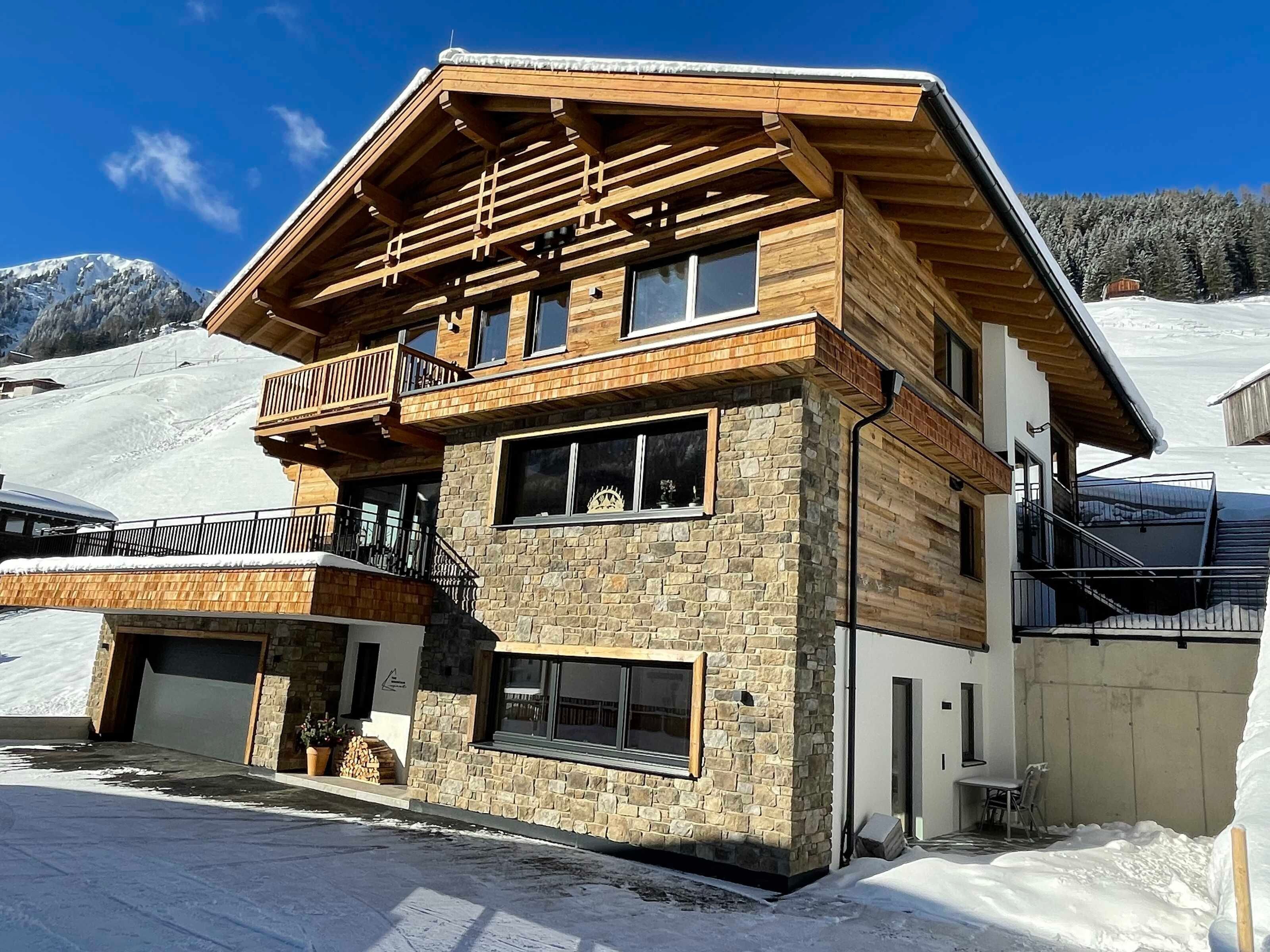 Un chalet en bois à deux étages, avec des murs en pierre, un balcon et un télésiège en arrière-plan.