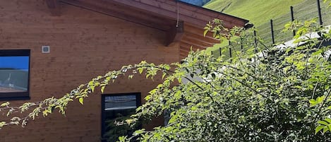 Un edificio moderno con techo inclinado, rodeado de vegetación exuberante y montañas al fondo.
