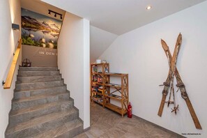 A staircase leading to a room with a mountain landscape poster, a wooden bookshelf, and skis mounted on the wall.