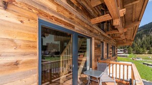 A wooden cabin with a balcony, large sliding glass doors, and a view of a forested valley. - Apartment Enzian - TUX MOUNTAIN apart (Juns)