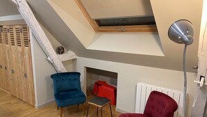 A room with a sloped ceiling, a skylight, a red chair, a blue chair, a small table, and a radiator. - Adorable apartment located in a castle (AVOINE)