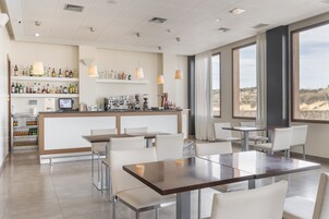 Zona de bar moderna con una barra larga, sillas blancas y vistas al desierto a través de amplios ventanales.