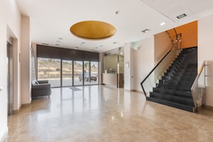 Un vestíbulo amplio con una recepción, una escalera y un gran ventanal con vistas al exterior.