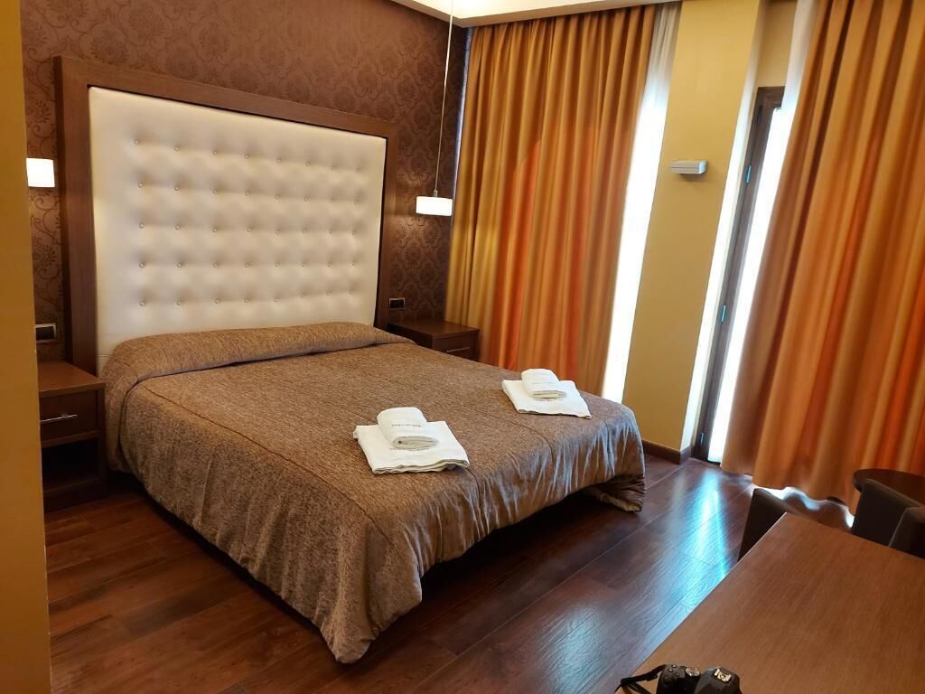 Een hotelkamer met een groot gestoffeerd hoofdeinde, een houten bed, twee handdoeken op het bed, een nachtkastje van hout en een houten tafel.