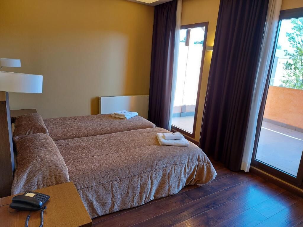 A hotel room with two beds, a bedside table with a phone, and a window with curtains.