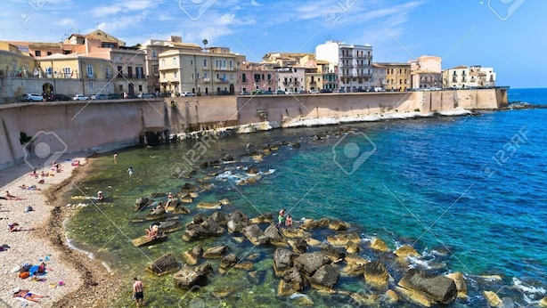 A coastal town with buildings along the sea, clear waters, and rocky areas. - Apartment with Hotel treatment (SIRACUSA)