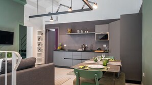 A modern kitchen with grey cabinets, a built-in oven, and a dining area with a table set for two. - Apartment with Hotel treatment (SIRACUSA)