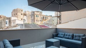A rooftop terrace with outdoor seating, a large umbrella, and a view of surrounding buildings. - Apartment with Hotel treatment (SIRACUSA)