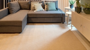 A modern living room with a grey sectional sofa, patterned cushions, a woven rug, and a small white table with potted plants. - Apartment with Hotel treatment (SIRACUSA)