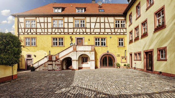 A traditional half-timbered building with a cobblestone courtyard, a staircase leading to the entrance, and a clear blue sky. - Hotel Wiener Botschaft (Veitshoechheim)