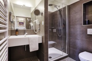 A modern bathroom with a glass-enclosed shower, a white sink with a towel, and a toilet. - Hotel Wiener Botschaft (Veitshoechheim)