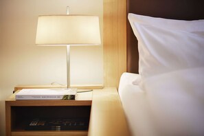 A neatly made bed with white sheets, a bedside lamp, and a small wooden nightstand with a book and remote control. - Hotel Wiener Botschaft (Veitshoechheim)