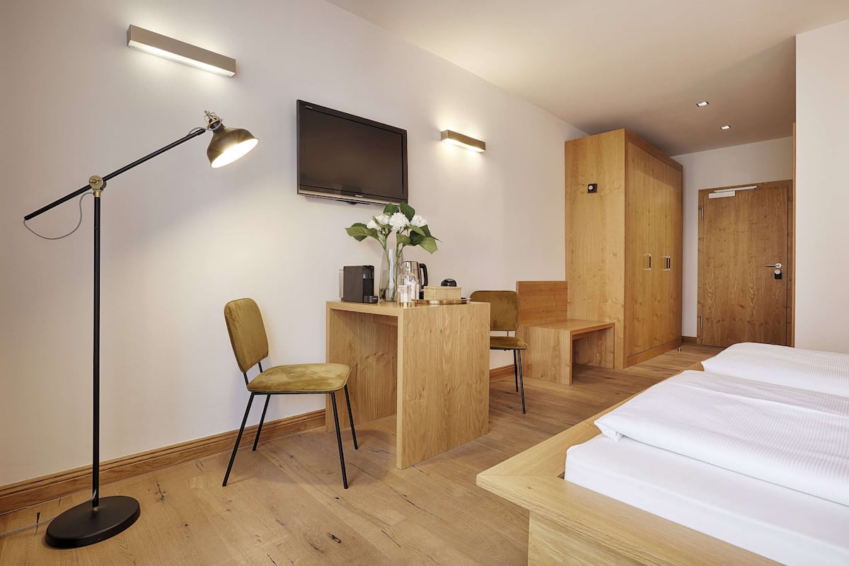 Quarto de hotel com cama, escrivaninha, cadeira e televisão.