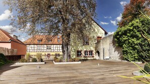 A courtyard with a wooden deck, a large tree, and traditional buildings with stone walls and timber framing. - Hotel Wiener Botschaft (Veitshoechheim)
