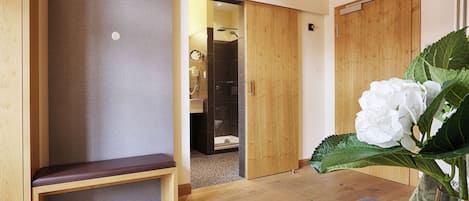 Un banco de madera, una puerta de madera y una flor blanca en una habitación con suelo de madera.