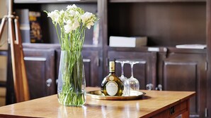 A wooden table with a clear glass vase containing white flowers, a bottle of wine, and two wine glasses on a tray. - Hotel Wiener Botschaft (Veitshoechheim)