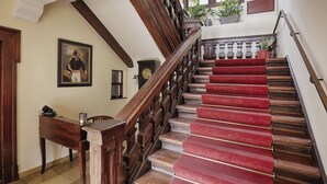 A grand staircase with a red carpet, wooden balusters, and a clock on the wall. - Hotel Wiener Botschaft (Veitshoechheim)