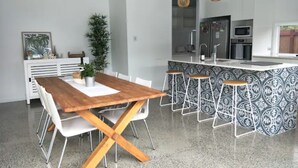 A modern kitchen with a central island, white bar stools, and pendant lighting. - The Family Beach House (Casuarina)
