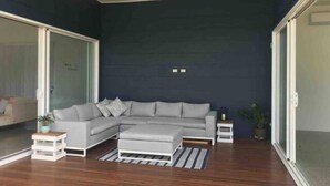 A modern living room with a grey sectional sofa, a white ottoman, and a ceiling fan. - The Family Beach House (Casuarina)