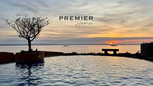 Une piscine à débordement offrant une vue sur le coucher de soleil, un arbre et un banc.