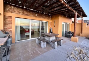 A patio with a stone table and benches, a barbecue grill, and a view through large sliding glass doors. - "Sunset Home" w/ Golf Cart & Beach Club Access (La Paz)