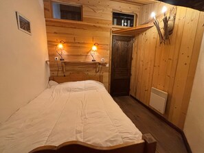 A wooden room with a bed, two wall-mounted lights, a door, and a small window.
