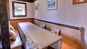 Comedor de madera con mesa y bancos, cuadros en la pared y ventana con vista a árboles.