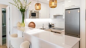 A modern kitchen with a large island, white cabinetry, stainless steel appliances, and two bar stools.