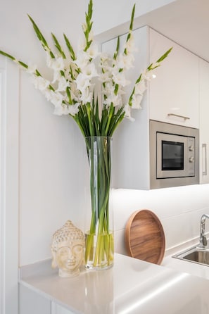 Una cocina con encimera blanca, un florero con flores blancas, una estatua de Buda y un cuenco de madera.