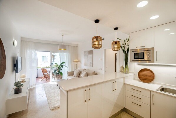 A modern kitchen with white cabinetry, a central island, pendant lighting, and a microwave.