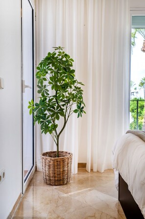 Una habitación con una cama, una planta en maceta, una ventana con cortinas y una puerta.