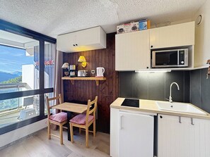 A compact kitchenette with a microwave, sink, and a small refrigerator. There is a wooden table with chairs and a window offering a view of the outdoors.