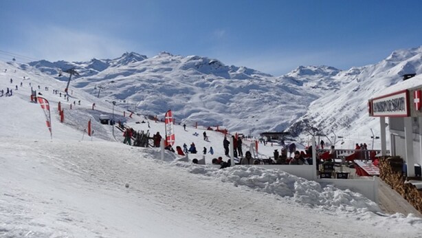 Pista de esquí nevada con un telesilla y un edificio con un letrero.