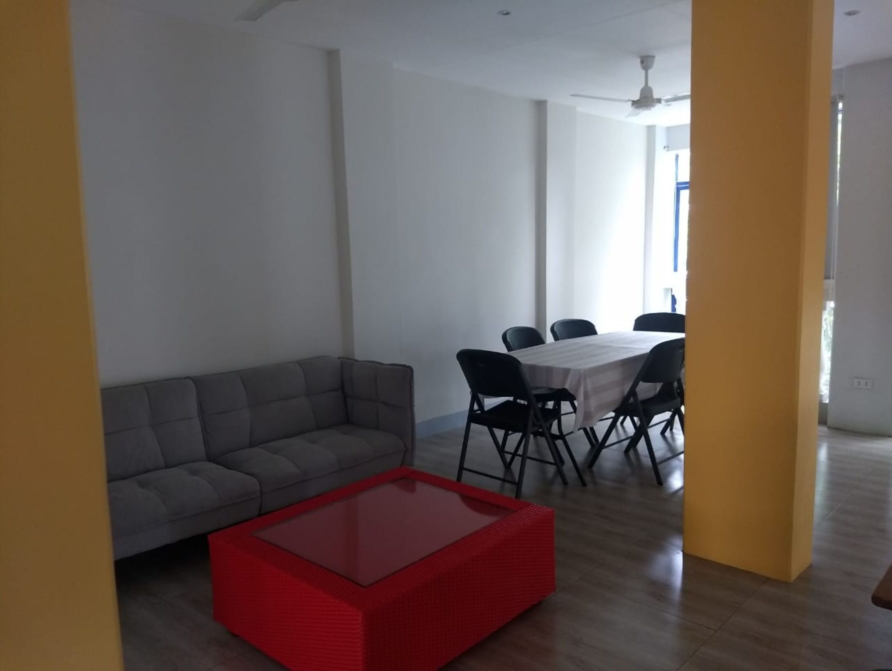 Una sala de estar moderna con un sofá gris, una mesa de centro roja y un comedor con una mesa blanca y sillas negras.