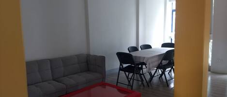Una sala de estar moderna con un sofá gris, una mesa de centro roja y un comedor con una mesa blanca y sillas negras.