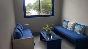 Un petit salon moderne comprenant un canapé et un fauteuil, une table basse avec un plateau en verre et une plante en pot.
