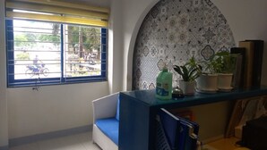 Une pièce avec un canapé bleu, un mur à motifs, une fenêtre avec des barreaux et une étagère remplie de livres et de plantes.