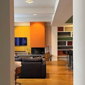 A modern living room with a fireplace, a flat-screen TV mounted on a yellow wall, and a wooden floor.