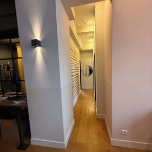 A hallway with a wooden floor, white walls, and a round mirror on the wall.